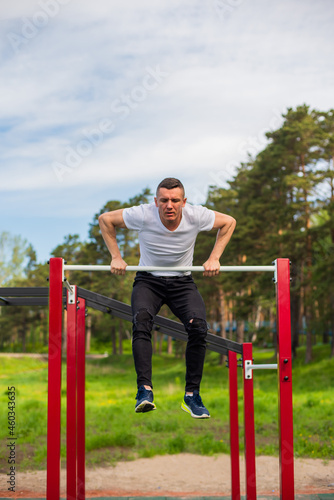 Caucasian man pulls himself up on a horizontal bar on a sports ground.