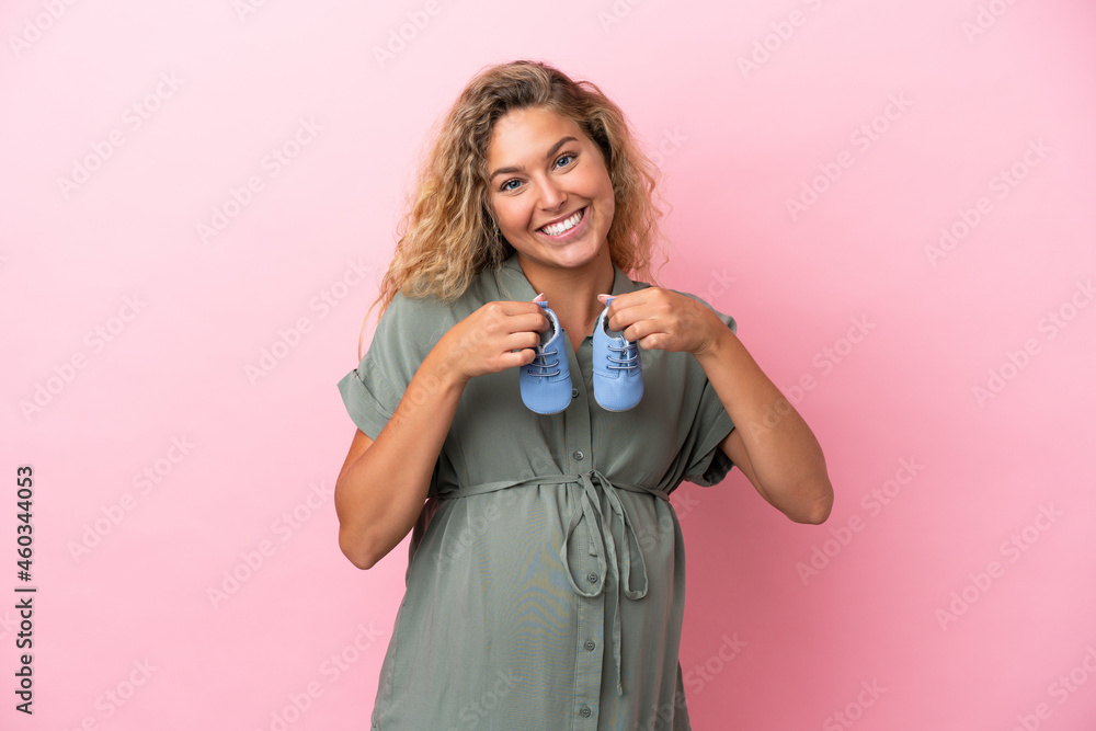 Girl with curly hair isolated on pink background pregnant and holding baby booties Girl with curly hair isolated on pink background pregnant and holding baby booties