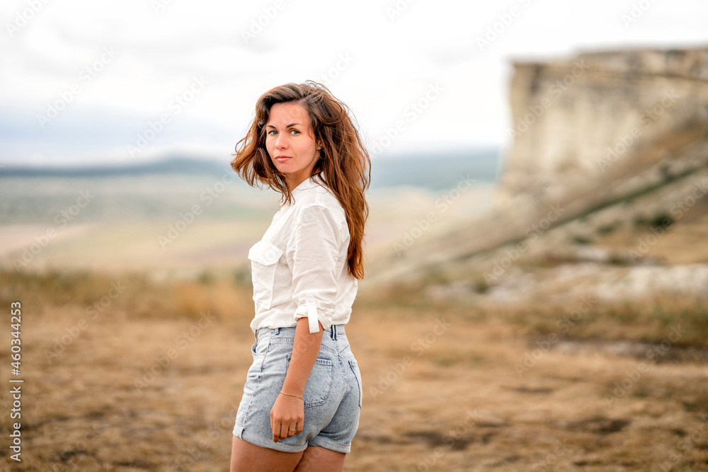 Portrait of a beautiful young woman in a white shirt on the edge of a cliff with an endless panorama, White Rock in the Crimea. The concept of travel Portrait of a beautiful young woman in a white shirt on the edge of a cliff with an endless panorama, White Rock in the Crimea. The concept of travel