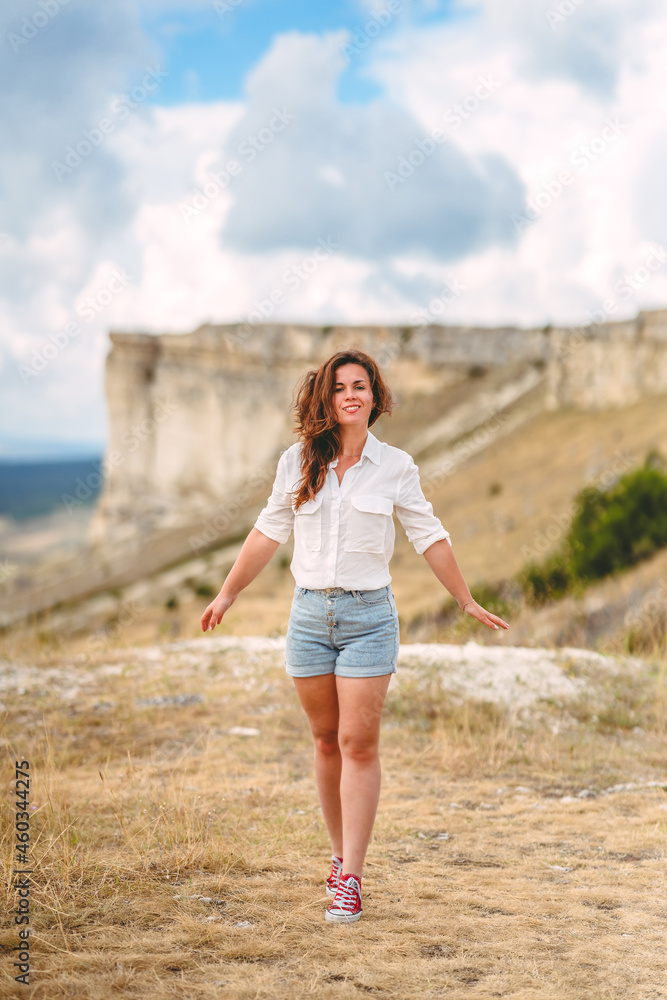 Portrait of a beautiful young woman in a white shirt on the edge of a cliff with an endless panorama, White Rock in the Crimea. The concept of travel