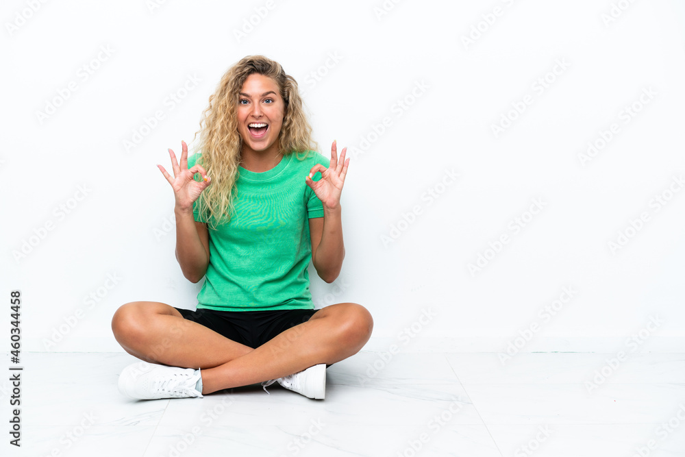 Girl with curly hair sitting on the floor showing an ok sign with fingers Girl with curly hair sitting on the floor showing an ok sign with fingers