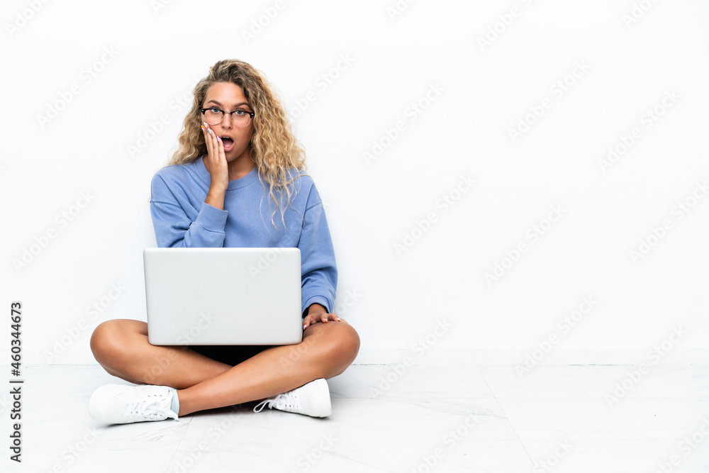 Girl with curly hair with a laptop sitting on the floor surprised and shocked while looking right Girl with curly hair with a laptop sitting on the floor surprised and shocked while looking right