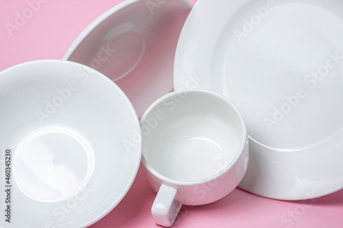A set of white dishes on a pink background. A set of plates, saucers and cups.