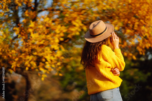 Stylish woman walking on park, wearing yellow sweater and cute trendy hat. Fashion, style concept. People, relaxation and vacations concept.