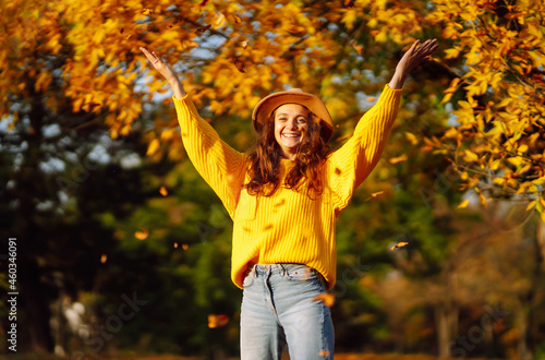 Stylish woman walking on park, wearing yellow sweater and cute trendy hat. Fashion, style concept. People, relaxation and vacations concept.