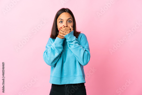 Young latin woman isolated on pink background covering mouth and looking to the side © luismolinero