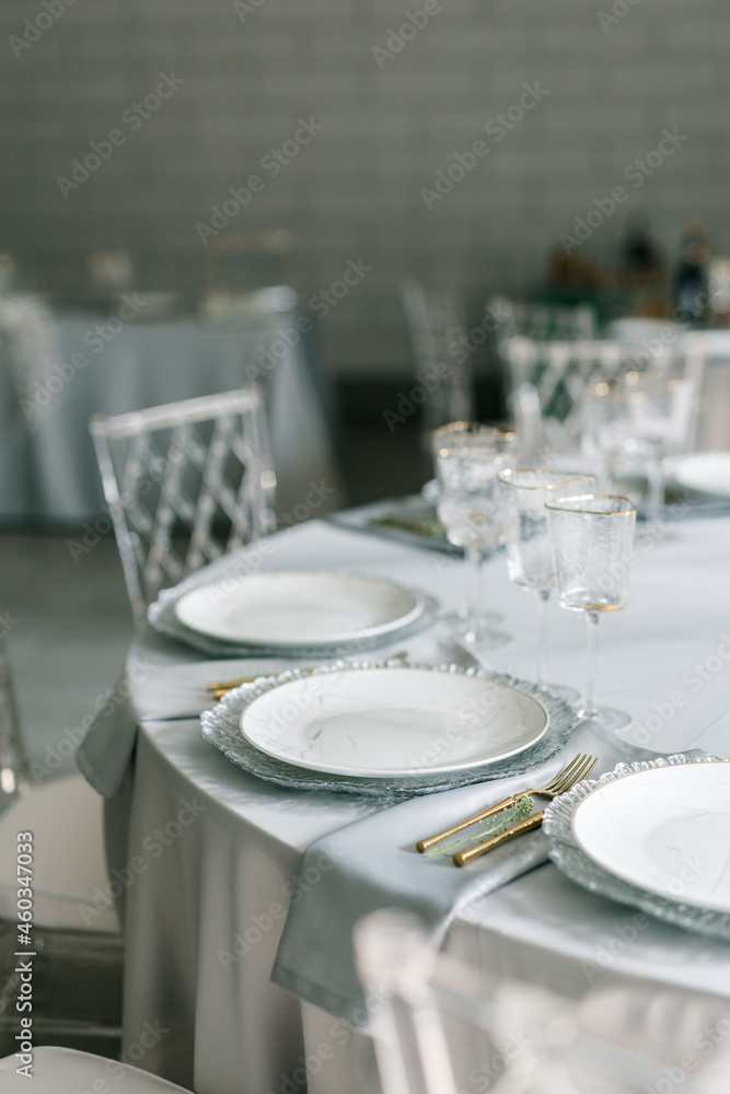 glass glasses and white plates. table setting in the interior of the restaurant. The decor of the festive table. In gray-silver tones with gold cutlery. Luxury wedding, party, birthday. glass glasses and white plates. table setting in the interior of the restaurant. The decor of the festive table. In gray-silver tones with gold cutlery. Luxury wedding, party, birthday.