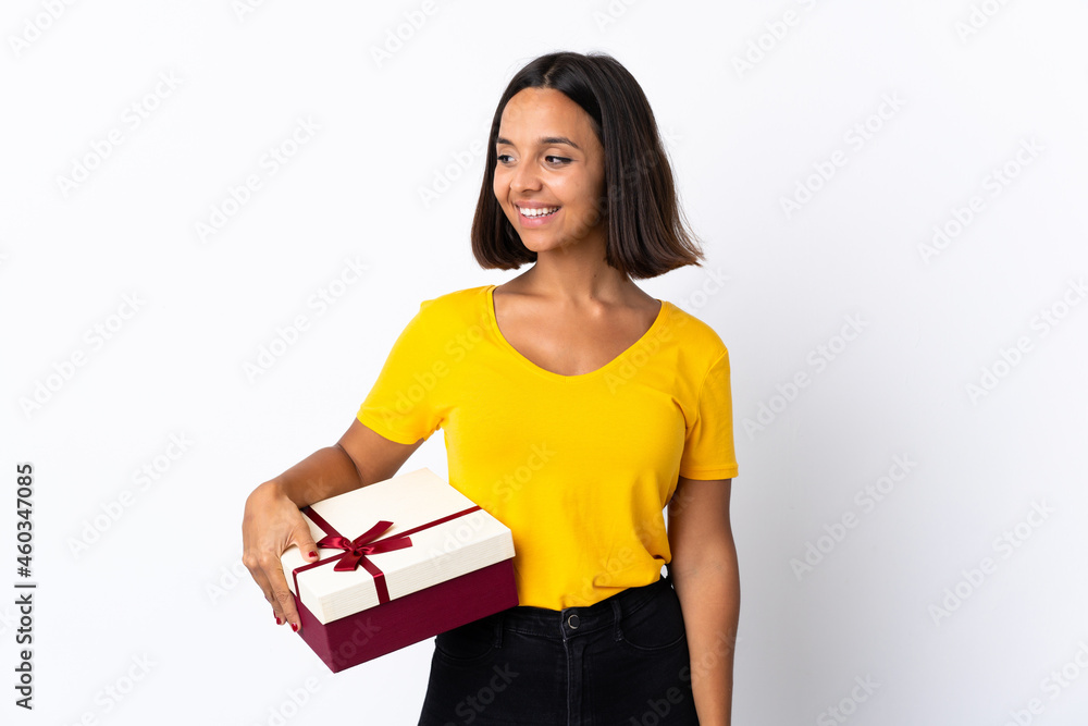 Young latin woman holding a gift isolated on white background looking to the side and smiling Young latin woman holding a gift isolated on white background looking to the side and smiling
