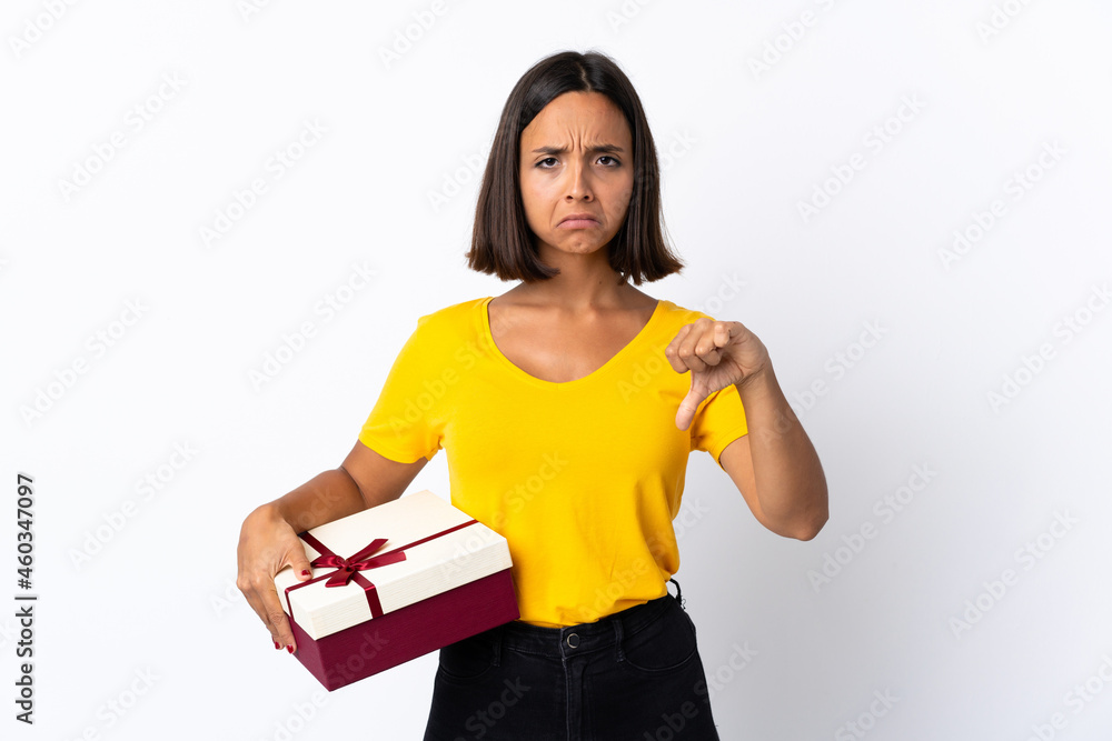 Young latin woman holding a gift isolated on white background showing thumb down with negative expression Young latin woman holding a gift isolated on white background showing thumb down with negative expression