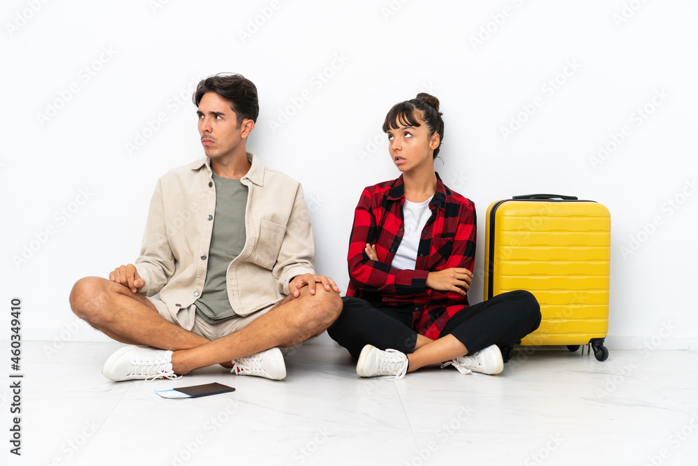 Young mixed race travelers couple sitting on the floor isolated on white background with confuse face expression while bites lip Young mixed race travelers couple sitting on the floor isolated on white background with confuse face expression while bites lip