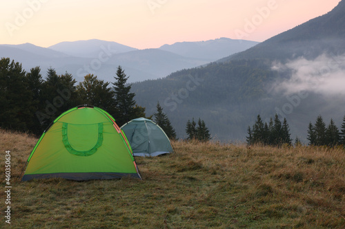 Picturesque view of mountain landscape with fog and camping tents in early morning