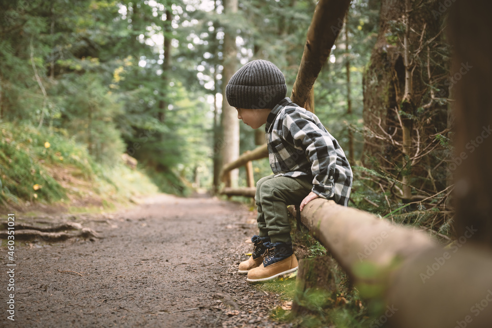 Small kid in a plaid shirt and gray hat in the forest. Childhood with nature loving concept