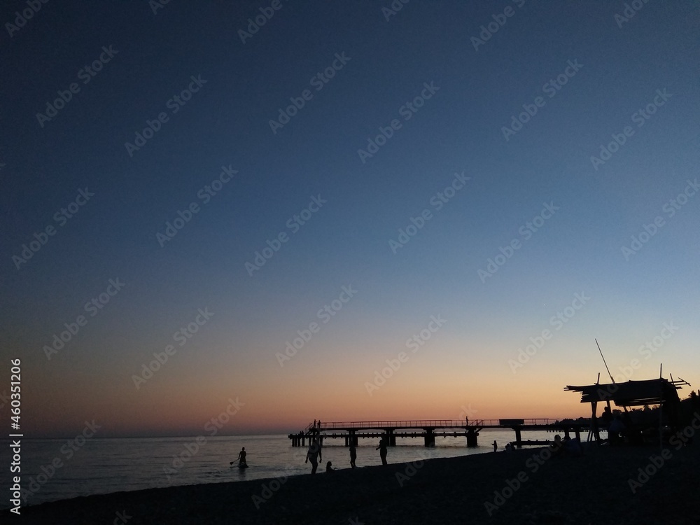 Sunset on the sea. Blue-orange. People and pier, contrasts.