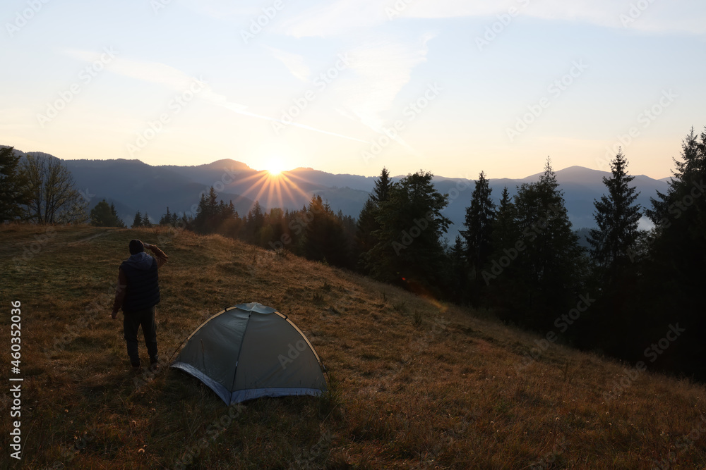 Tourist enjoying sunrise near camping tent in mountains, back view