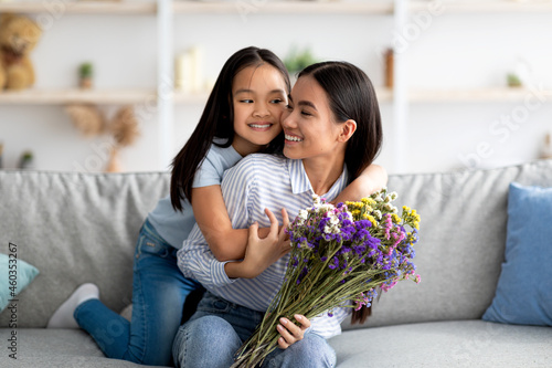 I love you, mommy. Excited asian girl greeting mom with birthday or mother's day, giving her flowers and embracing photo