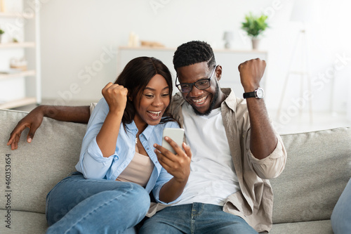 African american couple using cellphone, celebrating win