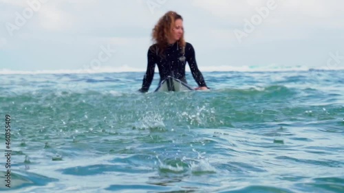 Video footage of surfer girl on white surf board in blue ocean pictured from the water in Bali
