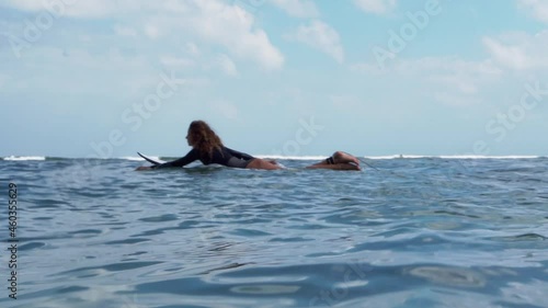 Video footage of surfer girl on white surf board in blue ocean pictured from the water in Bali