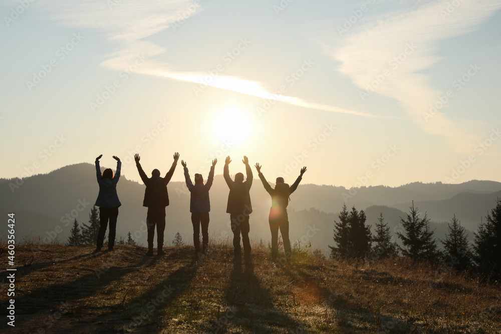 Group of people enjoying sunrise in mountains, back view