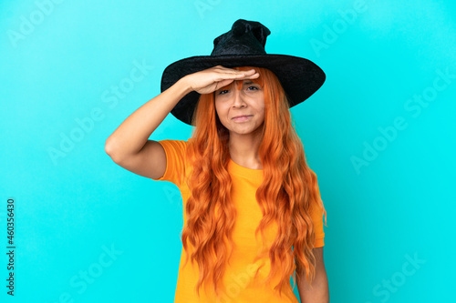 Young woman disguised as witch isolated on blue background looking far away with hand to look something © luismolinero