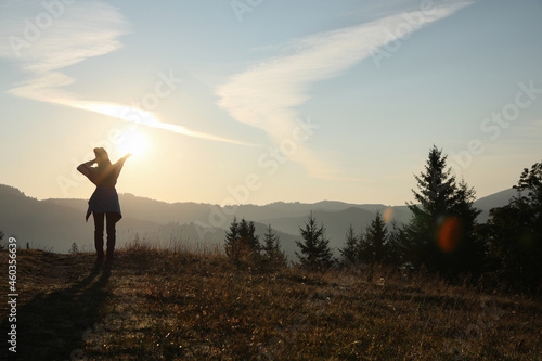 Woman enjoying sunrise in mountains, back view. Space for text