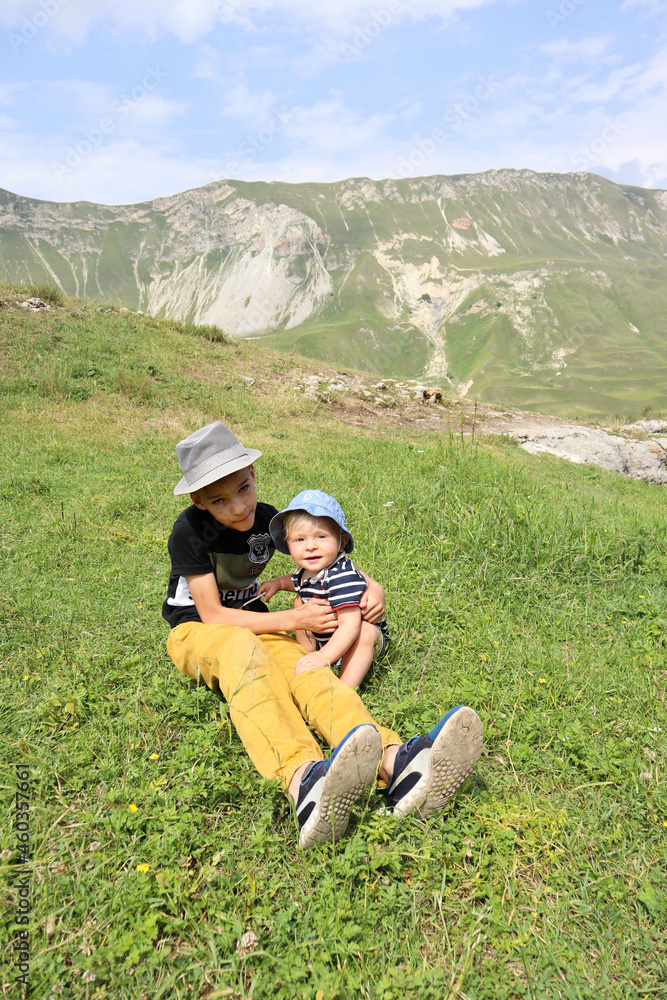 two brothers - big and small have a rest sitting on the grass in the beautiful mountains