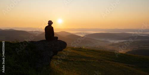 Alone tourist on the edge of the mountain hill against the backdrop of an incredible sunset mountains landscape