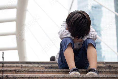 Homeless Asian child sitting alone on the stairway in the street. Poor, sad, scared and alone.