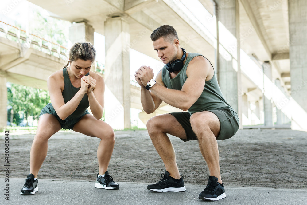 Athletic couple doing squats during street workout Athletic couple doing squats during street workout
