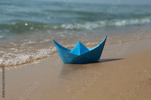 Blue paper boat on sandy beach near sea