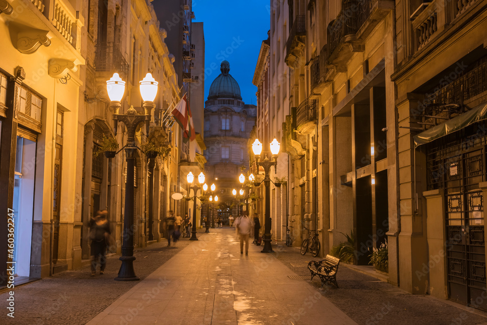 City of Santos, old town, Rua XV de Novembro in the early evening. In the background, the building of the Bolsa Oficial do Café in eclectic architecture. Street lit with yellow lights, cast iron poles