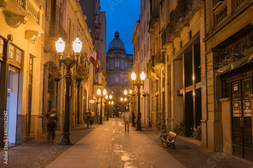 City of Santos, old town, Rua XV de Novembro in the early evening. In the background, the building of the Bolsa Oficial do Café in eclectic architecture. Street lit with yellow lights, cast iron poles