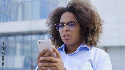 Scared young afro-american woman reading message on smartphone, confused face expression. Nervous black female facing cyber bullying in social media. Distressed company employee having panic attack