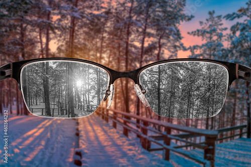 Looking through glasses to black and white sunset in winter forest view focused in women's glasses. Color blindness. World perception during depression. Medical condition. Health and disease concept.