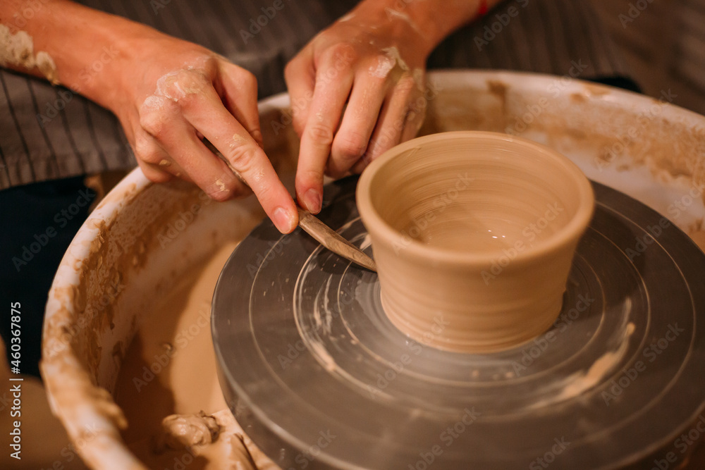 Men's hands are large, they decorate a mug of clay on a pottery table with a knife. Removes excess pieces of clay with a stack Men's hands are large, they decorate a mug of clay on a pottery table with a knife. Removes excess pieces of clay with a stack