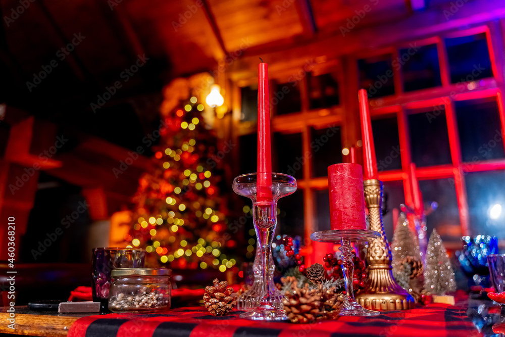 Cozy living room with Christmas decorations at the table. Christmas decorated room with many lights, candles and red light. Room with armchairs and carpet