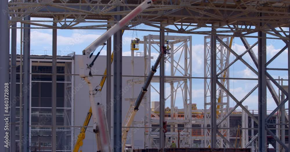 At the construction site of the plant under construction, there are many cranes and hoists, so far there are only frames made of metal beams against the background of a blue sky At the construction site of the plant under construction, there are many cranes and hoists, so far there are only frames made of metal beams against the background of a blue sky