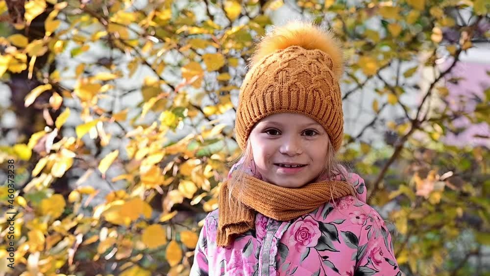 A cute little girl walks on the street in the autumn park. Portrait of a smiling girl on a background of orange leaves. Autumn mood. Outdoor walks and games with children. High quality FullHD footage A cute little girl walks on the street in the autumn park. Portrait of a smiling girl on a background of orange leaves. Autumn mood. Outdoor walks and games with children. High quality FullHD footage