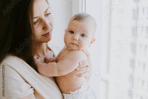 a small child in a young mother's arms looks directly at the camera and smiles sweetly happy family in the house copy space 