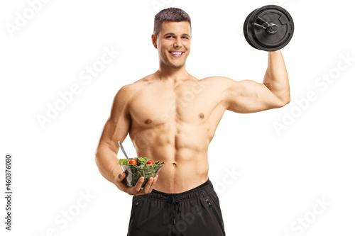 Shirtless musuclar young man holding a salad and lifting weights photo