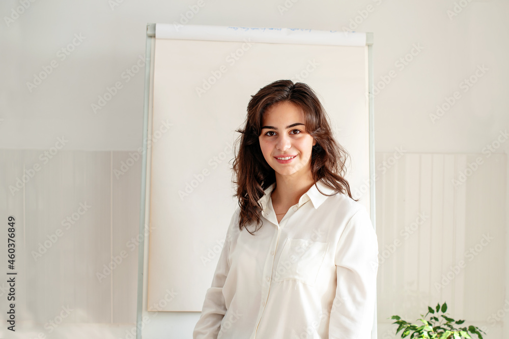 Portrait of young woman posing near blank empty whiteboard. Presentation concept. Teacher in white, businesswoman standing with a marker near a whiteboard, Online classes, business training 