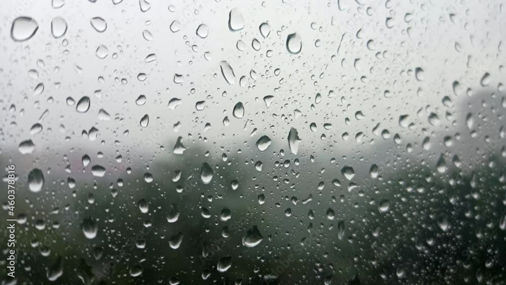 Close up image of rain drops falling on a glass. Blurred trees move with the wind in the background. Cloudy rainy weather, view from the window. Sadness, longing, despondency, autumn depression, gloom Close up image of rain drops falling on a glass. Blurred trees move with the wind in the background. Cloudy rainy weather, view from the window. Sadness, longing, despondency, autumn depression, gloom