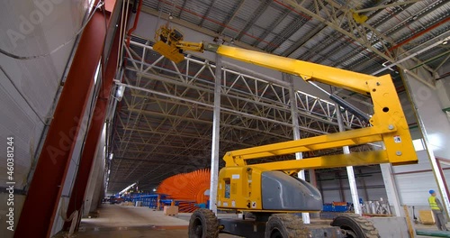 In a workshop under construction, car lifts raise workers in their cradle to the ceiling to perform work there