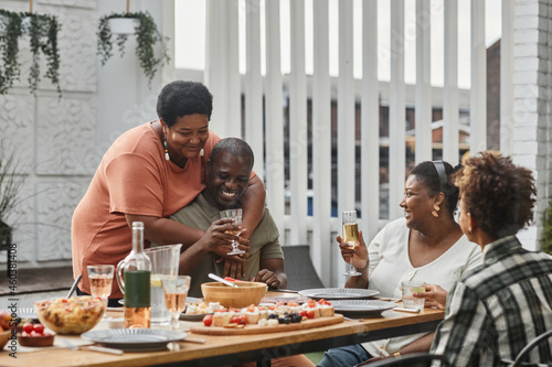Portrait of two generation African-American family enjoying dinner together with senior couple embracing in foreground, copy space