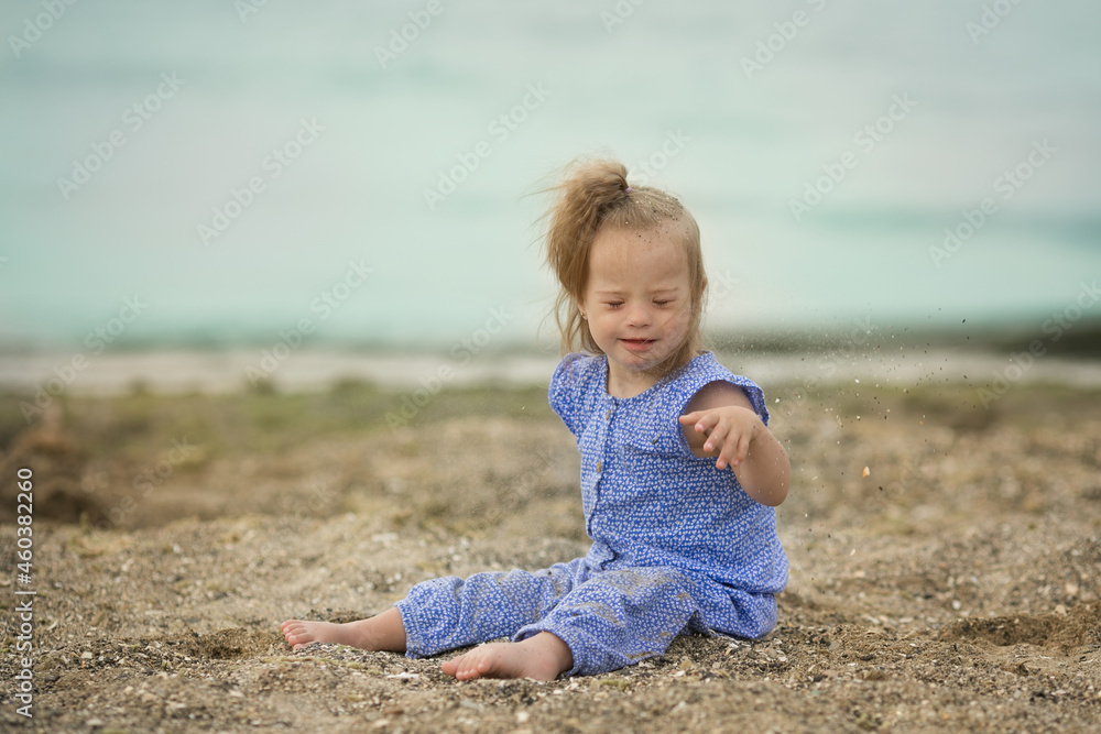 beautiful girl with Down syndrome throwing sand on the seashore beautiful girl with Down syndrome throwing sand on the seashore