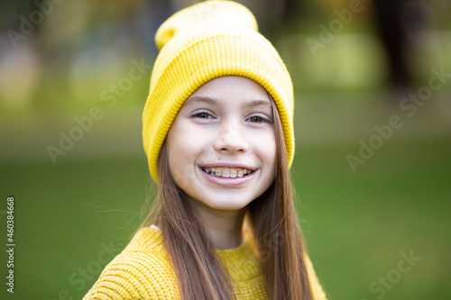 Portrait of modern happy teen girl with dental braces dressed in yellow clothes in park. Pretty teenage girl wearing braces smiling cheerfully. Kid girl in autumn smiling with braces teeth apparatus