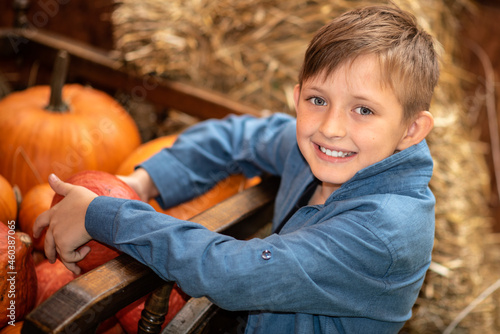 smiling boy sitting and holding pumpkins at the farm surrounded by many pumpkins in autumn