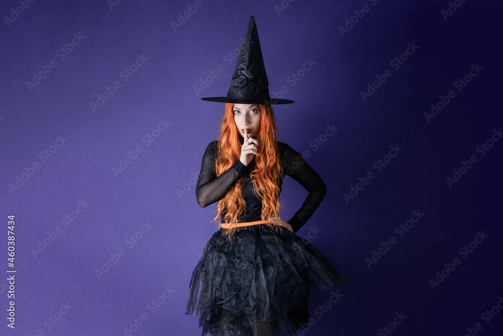 Young witch halloween costume purple wall background showing silence gesure