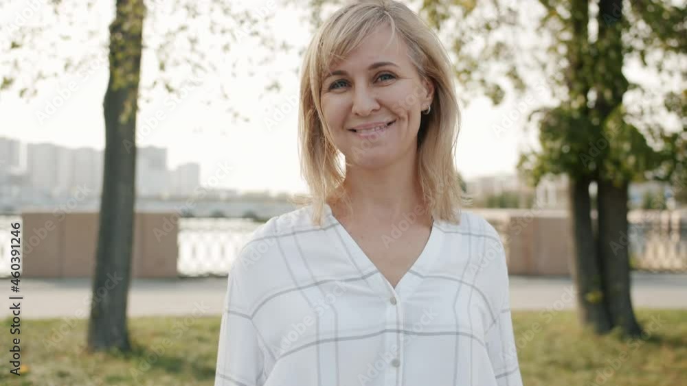 Slow motion portrait of happy middle-aged woman turning to camera and smiling standing in city street in summer. Positive emotions and people concept. Slow motion portrait of happy middle-aged woman turning to camera and smiling standing in city street in summer. Positive emotions and people concept.