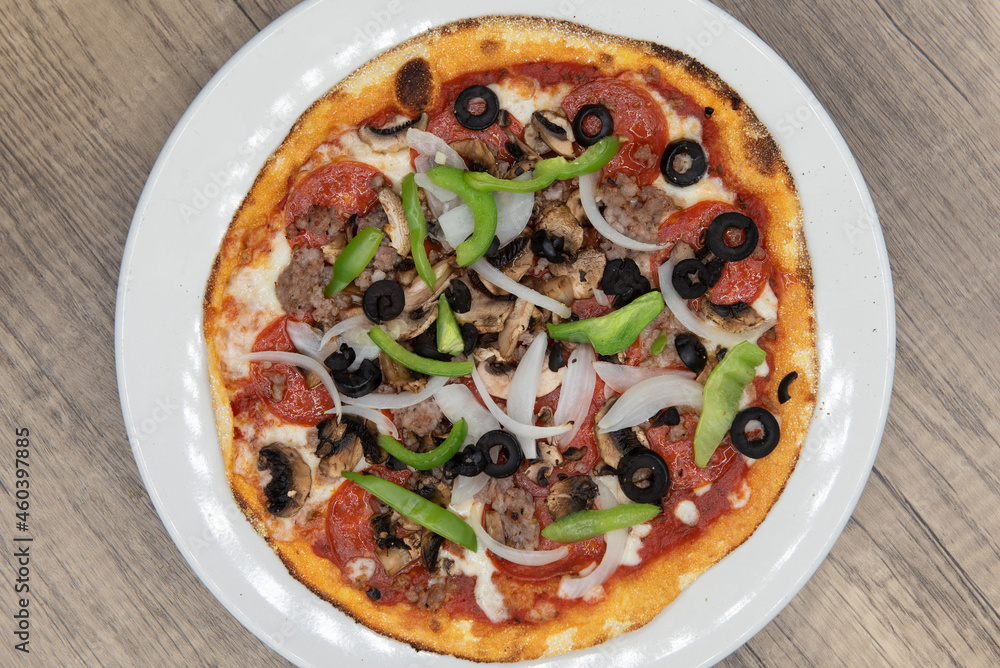 Overhead view of personal sized pizza with equal meat and vegetable toppings of olives, peperoni, sausage, and onions with a crispy crust Overhead view of personal sized pizza with equal meat and vegetable toppings of olives, peperoni, sausage, and onions with a crispy crust
